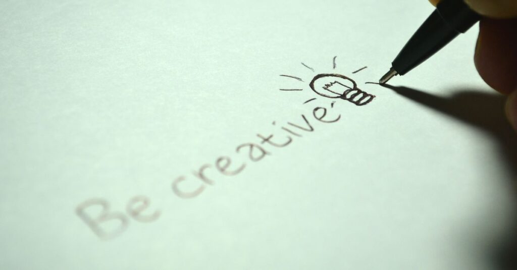Close-up of handwritten 'Be creative' with a light bulb sketch on paper.